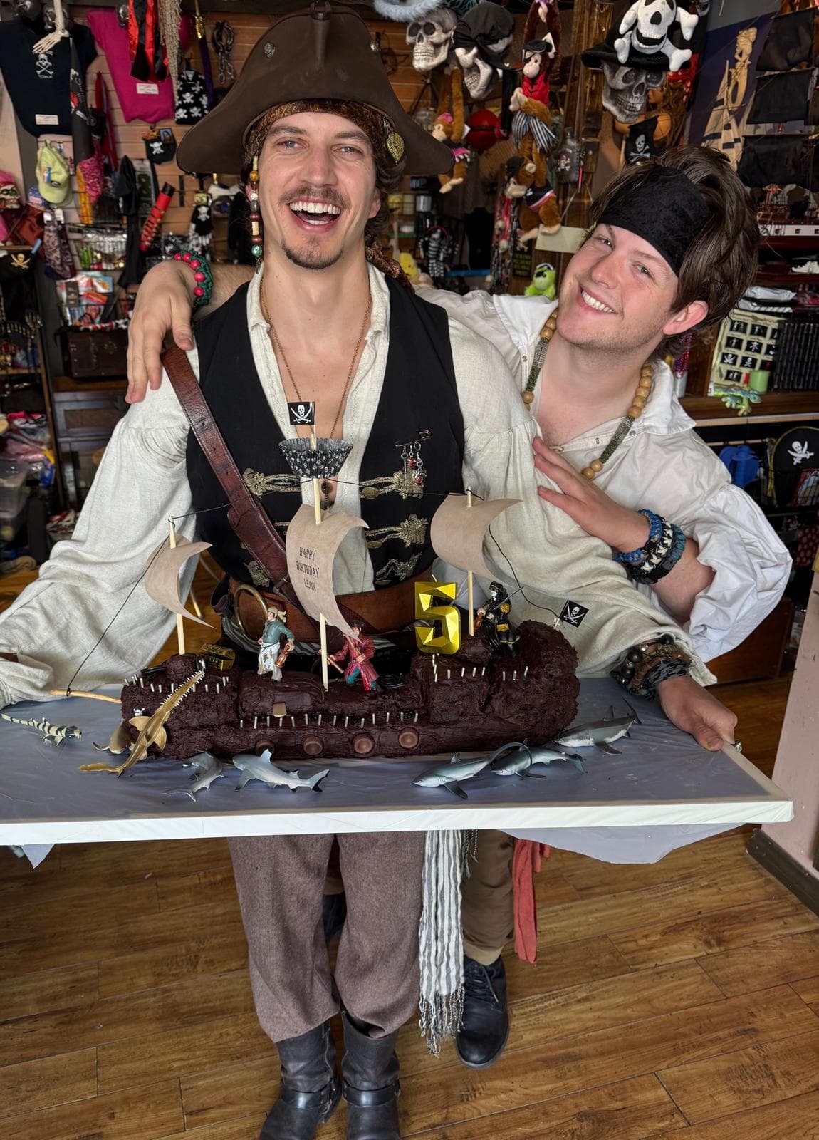 Two pirate hosts presenting a ship-shaped birthday cake inside the Pirate Shop